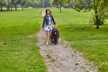 Genç bir kadın, parkta açık havada siyah bir tuğlayla yürüyor..
