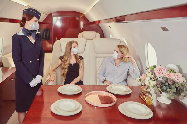 Хозяйка самолета в защитной медицинской маске обслуживает пассажиров в частном самолете. — стоковое фото