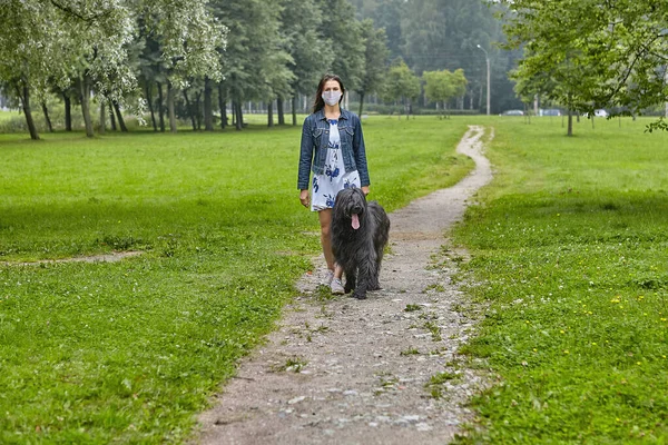 White woman walks with black briard in facial mask on open air. — Stock Photo, Image