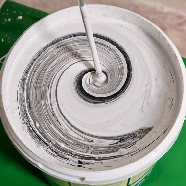 Ressam, yenileme sırasında duvarlar için boyaları sepette çırpıcı ile karıştırıyor..