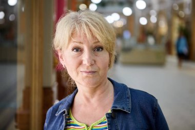 Sarı saçlı yaşlı kadın alışveriş merkezinde portre için poz veriyor. Güzel, yaşlı, beyaz kadın ticaret galerisinde duruyor..