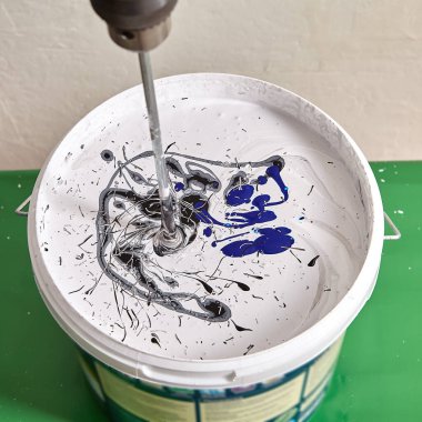 Tamirci, duvarı boyamak için yenileme sırasında mikserin yardımıyla sepette yeni renkler yapıyor. Ev ressamı boyaları matkapla karıştırıyor..