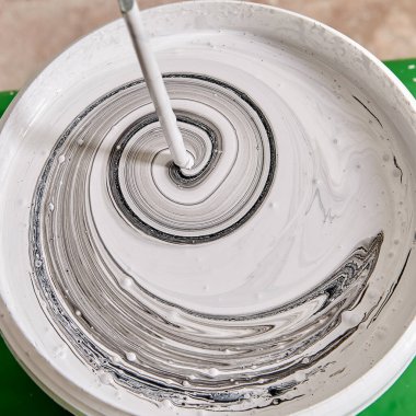 Ev boyacısı, boya duvarı tadilatı sırasında sepetteki çeşitli renkleri matkapla karıştırıyor. Tamirci boyaları mikserle karıştırıyor..