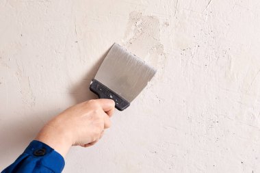 Sıvacı, küçük delikleri macun bıçağıyla doldurmak için ince yüzey dolgusu kullanır..
