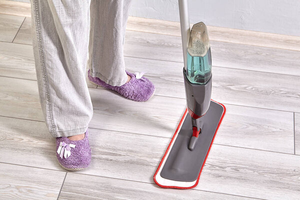 Flat microfiber spray mop for house cleaning with spraying water. Cleaning-lady cleans floor from dust and dirt.