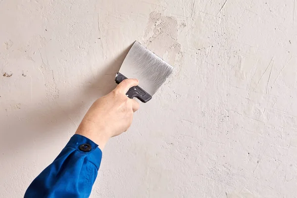 House painter putties the wall of the home with stucco and work tool during renovation. Handyman is finishing walls using putty.