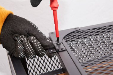 Alıcı, tornavida kullanarak TV standının metal çerçevesinin kapılarına vida sıkıyor..