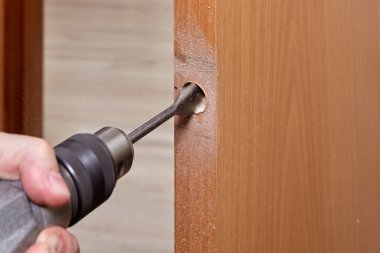 Çilingir kapı mandalı için delik açarken tahta parçası kullanır..