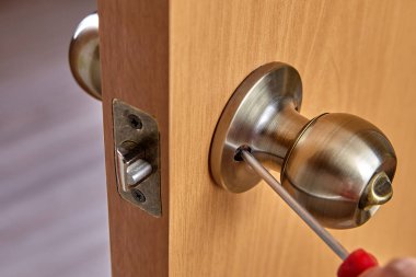 Locksmith fixes door handle rose with screw, using  screwdriver.