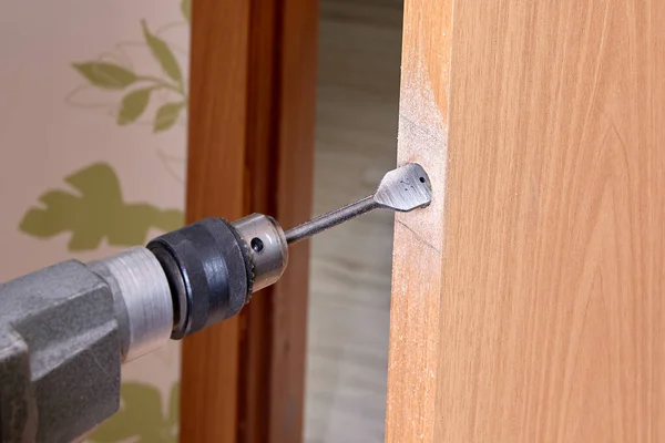 Locksmith with electric drill drilling hole for  door latch.