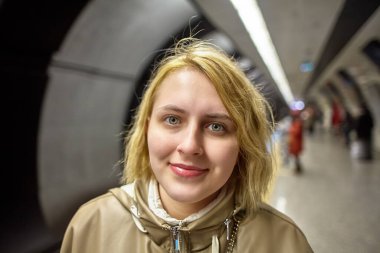 Genç Avrupalı bir kadın metro istasyonunun platformunda tren bekliyor..