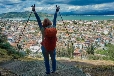 Hiker or backpacker raised his hands with walking poles, standing over panorama of Fethiye town and resort in Turkey in springtime.