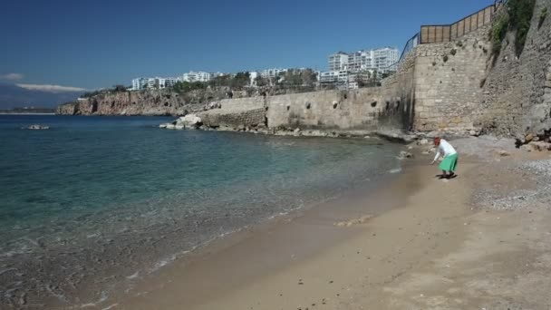 Genç bir kadın deniz dalgasının sıcaklığını ölçmeye çalışıyor ama baharın başında Antalya, Türkiye 'de ücretli bir plajda ayakkabılarını ıslatmaktan korkuyor.. — Stok video