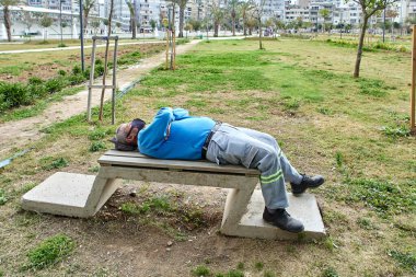 Yüz maskesi takan bir kamu görevlisi bahar zamanı öğleden sonra bankta uyuyakaldı..