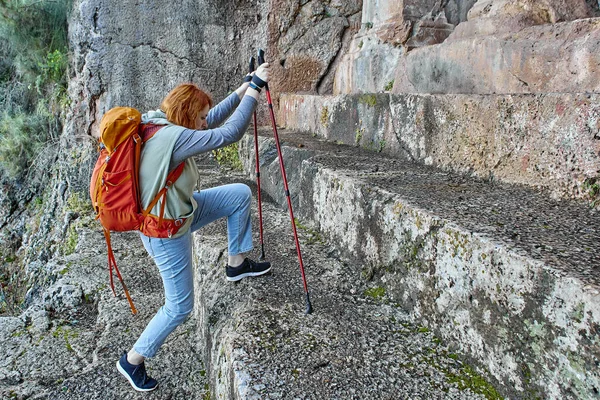 Tourist walking around Fethiye in Turkey, young European woman climbs stairs to Amyntas Rock Tombs using hiking poles. — Stock Photo, Image