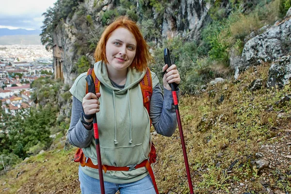 Young white woman walks along cliff with ancient Lycian tombs using hiking poles. — Foto de Stock