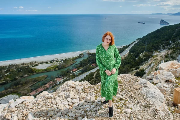 European young woman in green summer dress pozuje dla fotografa na skale nad morzem wczesną wiosną Antalya, Turcja. — Zdjęcie stockowe