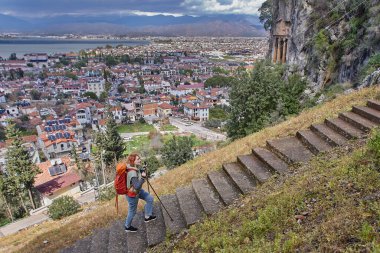 Sırt çantası ve yürüyüş direkleri taşıyan yürüyüşçü, Türkiye 'nin Fethiye kentindeki Telmessos antik kentinde bulunan Amyntas taş mezarlarına merdivenlerden iniyor..