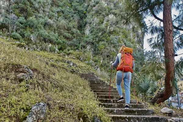 Tourist with backpack and walking poles climbs stairs to Lycian rock tombs in Fethiye, Turkey, in early spring. — Stock Photo, Image