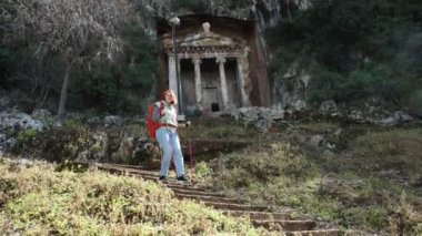 Avrupalı turist, Türkiye 'nin Fethiye kentindeki Lycian kaya mezarlarını bahar başında ziyaret ettikten sonra yamaçtan aşağı doğru yürüyor.