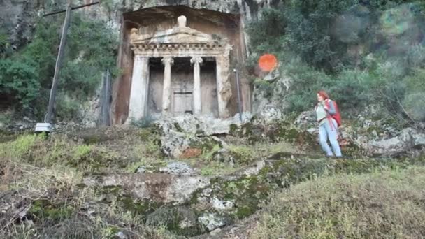 Redhead Caucasian woman walks downhill using trekking poles after visiting Amynthas Rock Tomb in Fethiye, Turkey. — Stock Video