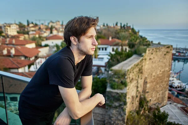 Slender European man, about 20 years old, sadly looks at old city in Antalya from observation point. — Stock Photo, Image