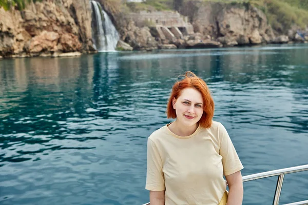 Tourist yacht sails past small waterfall, young European woman poses for photo. — Stock Photo, Image