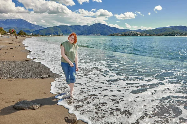 Camminando a piedi nudi sulla spiaggia bagnata sabbia sulla linea di surf, giovane donna europea passeggia vicino al mare. — Foto Stock