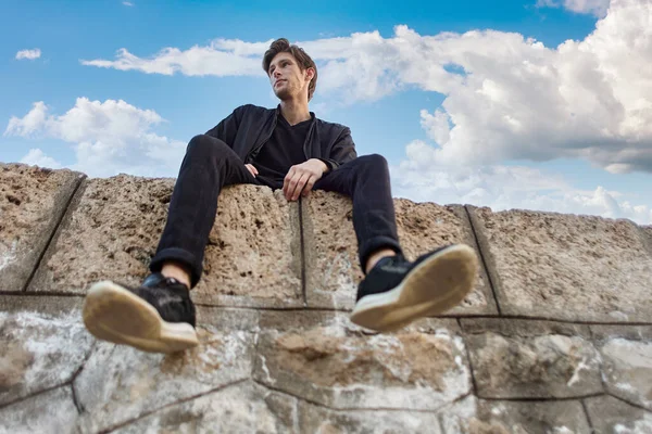 Vista inferior del hombre sentado en la pared de piedra. — Foto de Stock