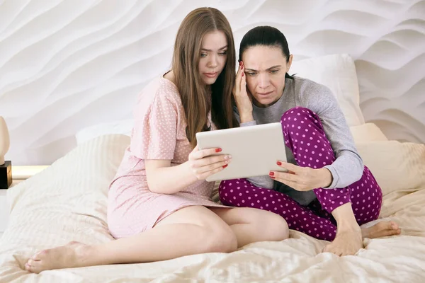 夜の服を着た女性がベッドルームに座っている間、電子タブレットの画面上で映画を見ています. — ストック写真