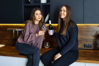 Kadınlar parti arifesinde mutfak tezgahında otururken şarap ve camla poz verirler..