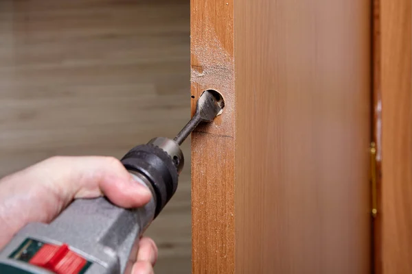 Locksmith drills hole for door lock with knob. — Stock Photo, Image