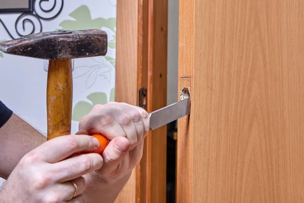 Locksmith uses chisel to cut grooves under plate of new door lock. — стоковое фото