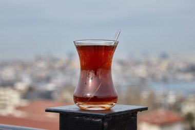 Glass of Turkish black tea sits on rooftop fence against backdrop of Istanbul cityscape.