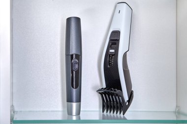 Clipper and trimmer to remove hair in nose are on shelf in locker of bathroom.