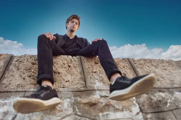 Young man looks down, sitting high on stone wall. — Foto de Stock