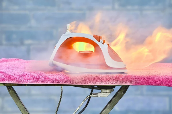 Ein überhitztes Haushaltsgerät brennt, vergessenes elektrisches Bügeleisen fängt auf Bügelbrett Feuer. — Stockfoto