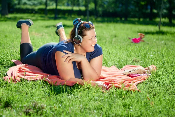 Fet vit kvinna ligger på magen på överkastet på gräsmattan av solig sommardag. — Stockfoto