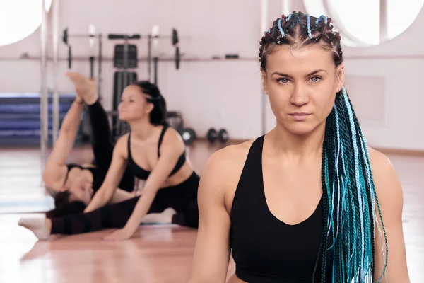 Cara séria de mulher treinador de fitness na frente de atletas que estão se aquecendo e fazendo alongamento. — Fotografia de Stock