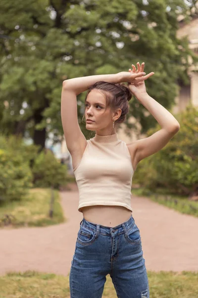 Mujer joven y delgada de 18 años se para en el parque con los brazos levantados. —  Fotos de Stock