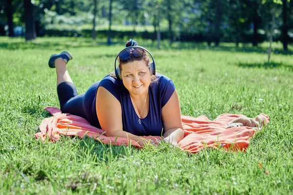 Fet kvinna vilar på gräsmattan liggande på magen. — Stockfoto