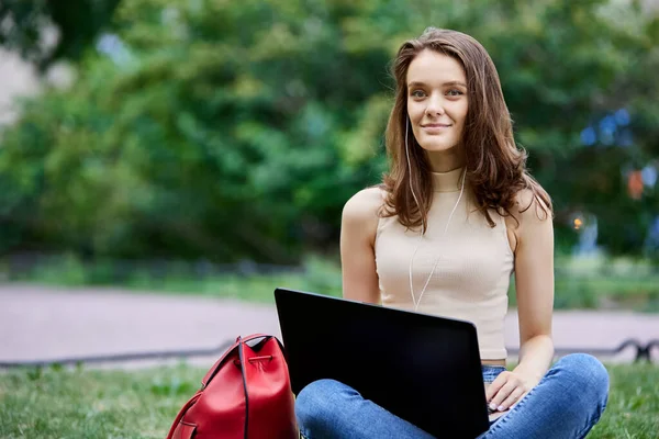 18-jährige Frau sitzt mit Laptop auf Rasen im Stadtpark. — Stockfoto