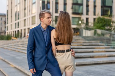 Takım elbiseli bir adam sokakta şortlu bir kıza sarılıyor..