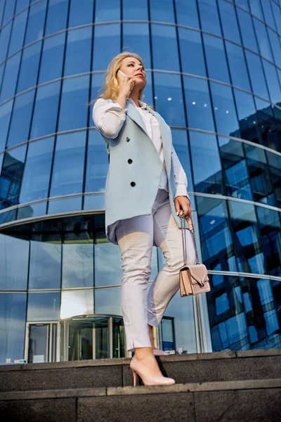 Młoda pewna siebie kobieta stoi w pobliżu centrum biznesowego i rozmawia przez smartfona. — Zdjęcie stockowe