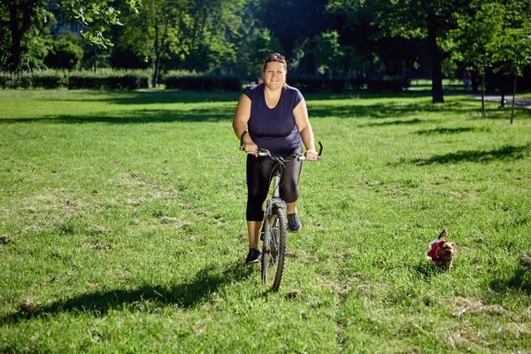 Junge gesunde Frau fährt mit kleinem Hund im Park Fahrrad. — Stockfoto