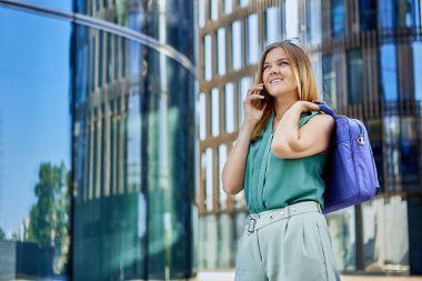 Neşeli, sıska kadın dışarıda telefonla arkadaşlarıyla konuşuyor..
