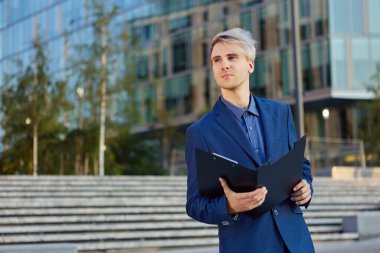 Düşünceli iş adamı iş merkezinin yakınında dosyasıyla dışarıda duruyor..