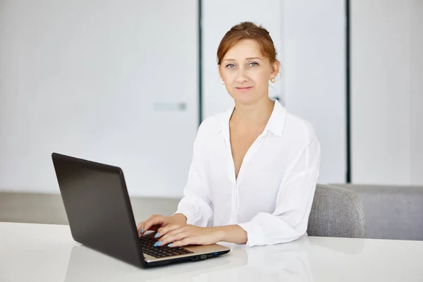 Впевнена молода жінка сидить в офісі і працює з ноутбуком . — стокове фото