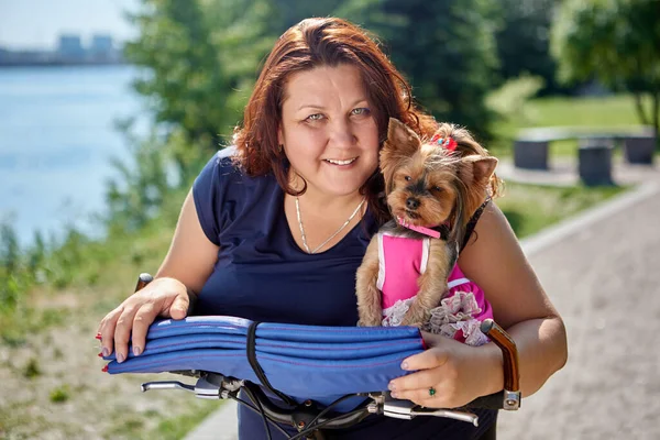 Túlsúlyos mosolygós nő yorkshire terrierrel a kezében a kertben. — Stock Fotó