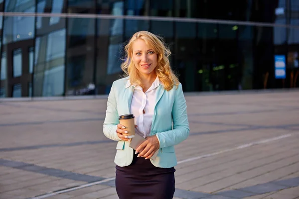 Cheerful businesswoman stands outdoors in business suit and with cup of coffee. — Fotografia de Stock